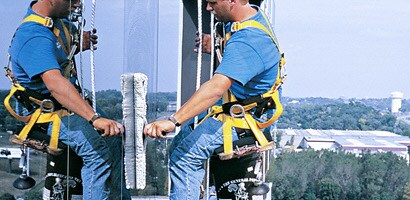 Window washer cleaning windows of tall building seated in suspension workseat
