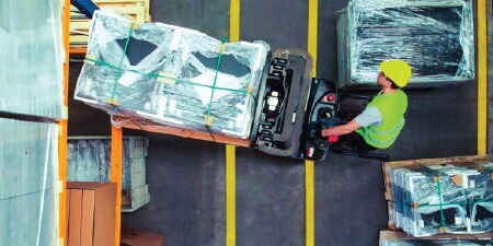 Overhead view of a forklift operator maneuvering a pallet across taped lane marks into a storage area
