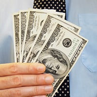 A man holds five 100-dollar bills in front of his tie.