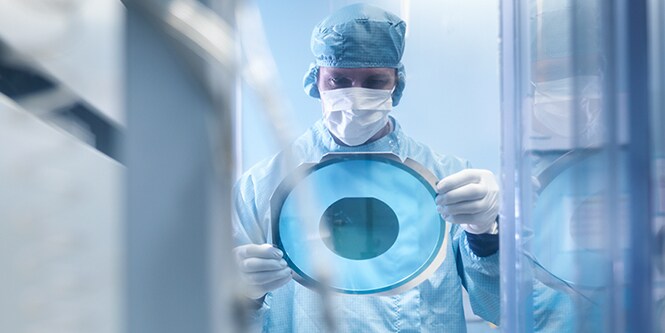 Man in scrubs holding clear blue disc from semiconductor process protection.

