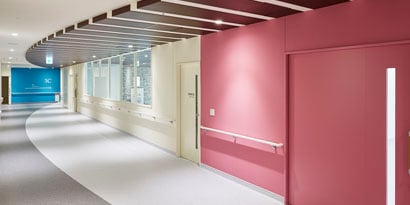 A hallway in a commercial building displays red, yellow and wood-grain finishes, including 3M™ DI-NOC™.
