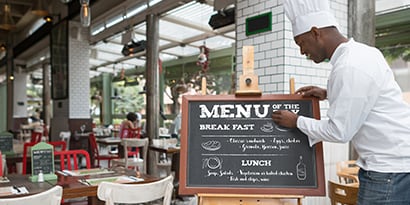 chef updating the chalk menu board displayed outside of a commercial restaurant

