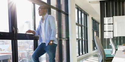 A man leans against a bank of windows in a commercial building, as the sun streams in.
