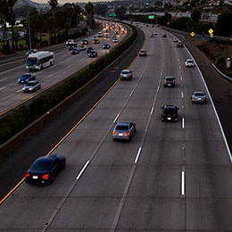 A busy eight-lane highway at dusk has easily viewable pavement markings.