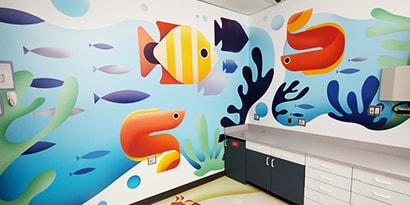 A wall has an interior graphics wrap with images of cheerful, brightly coloured fish.
