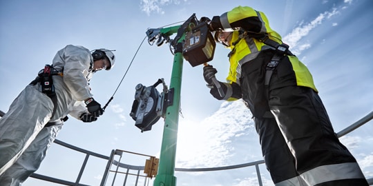 Two industrial workers in protective completing setup of confined space entry davit.
