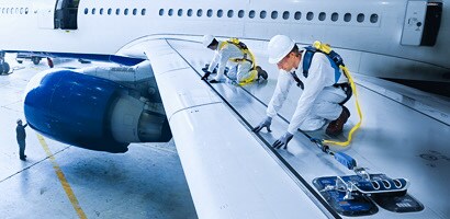 Workers on aircraft wing performing maintenance secured by fall protection gear
