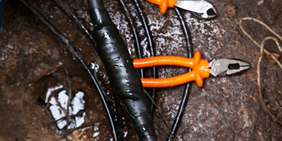 Electrical tape splice and orange electricians pliers in watery area.
