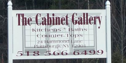 A big white sign wrapped in 3M coloured films that says The Cabinet Gallery and phone number in maroon font
