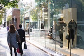People walking though an outdoor shopping mall by a glass display