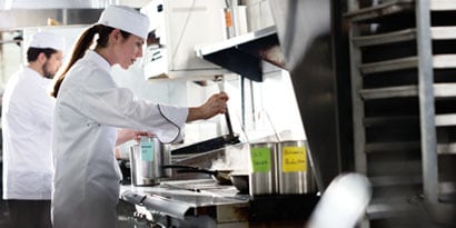 A chef cooks in front of steaming pans in a commercial kitchen.
