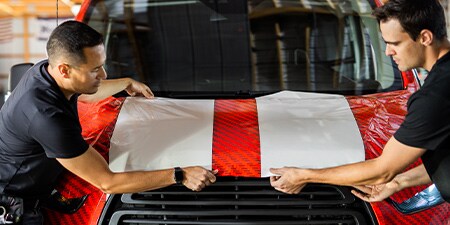 Two installers positioning IJ280 vehicle graphic film on hood
