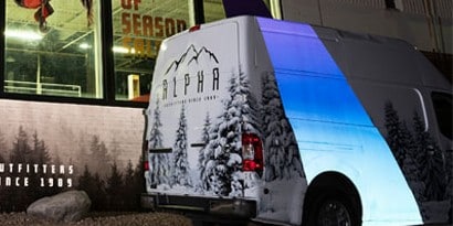 A graphic wrap on a van reflects blue and white light at night.
