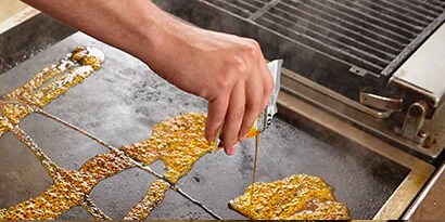 chef pouring Scotch-brite quick clean griddle liquid onto commercial stove top
