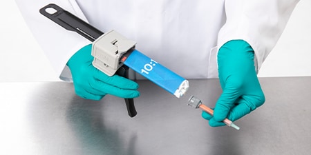A gloved worker attaches a mixing nozzle to a 10-to-1 Duo Pak adhesive held in an EPX applicator
