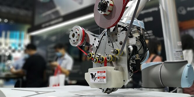 Closeup of a complex taping head attached to a robot arm and poised over a workpiece
