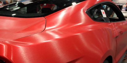 A red sports car has a red vehicle wrap with a textured overlaminates
