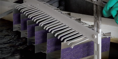 Image of masked metal plates on a rack as a worker is about to lower them into an anodizing solution.
