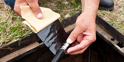 Image of 3M™ Scotch® Vinyl Mastic Tape 2200 wrapping a low voltage cable in an irrigation hole.
