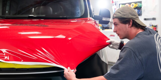 An individual installing printable wrap film onto the hood of a vehicle.