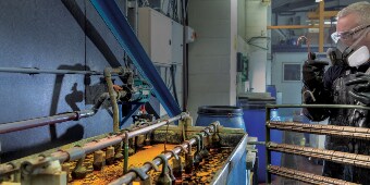 Image of a worker in protective gear preparing to hang a rack of parts in an electroplating bath
