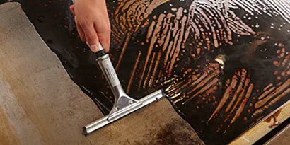 before and after shot of a dirty griddle being cleaned with a scotch-brite squeegee tool
