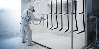 Image of a worker in protective gear applying powder coat paint to metal parts
