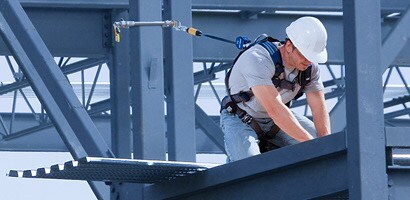 Worker kneeling on beam connected to fall protection anchor
