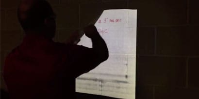 A technician demonstrates how to install a reflective graphic film wrap on a textured wall surface
