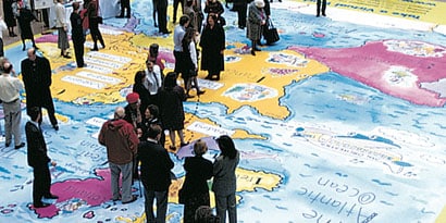 Dozens of people gather on a vivid floor wrap of a world map with overlaminate

