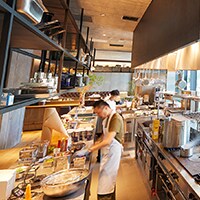 A busy, modern commercial kitchen has many dishes cooking.